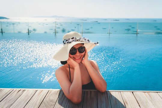 Sexy Woman in Swimsuit is Relaxing in Swimming Pool, Beautiful Asian Woman Wearing Straw Hat and Relax Sunbathe in Poolside on Summer Holiday at Resort Hotel, Leisure Activities and Relaxation Time