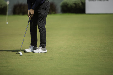 Golf player at the putting green hitting ball into a hole