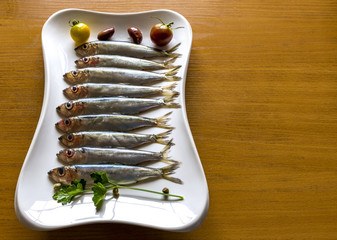 Raw Baltic herring sprats on white dish, served with vegetables and greens

