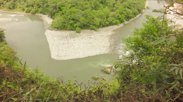 A high-angle view of the winding Mulatos River cutting through dense green jungle near Tena in the Ecuadorian Amazon, a rocky sandbar forming a natural island, thick vibrant vegetation around.