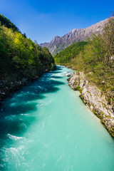 Famous river Soca near city of Kobarid. Beautiful emerald, green and blue wild river Soca, Julian alps, Slovenia. Blue sky, flowing alpine river, green trees and alpine peaks in background.