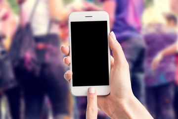 Woman's hands are holding a smartphone with a blank screen and a copy space and in the background a party for young people.