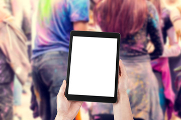 Woman's hands are holding a tablet with a blank screen and a copy space and in the background a party for young people.