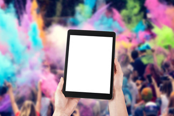 Woman's hands are holding a tablet with a blank screen and a copy space and in the background a party for young people.