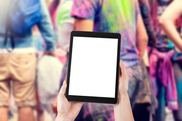 Woman's hands are holding a tablet with a blank screen and a copy space and in the background a party for young people.