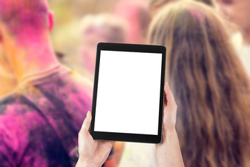Woman's hands are holding a tablet with a blank screen and a copy space and in the background a party for young people.