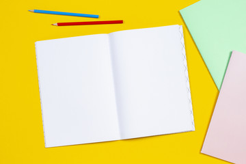 Open notebook colored pencils and colorful notebooks on yellow background