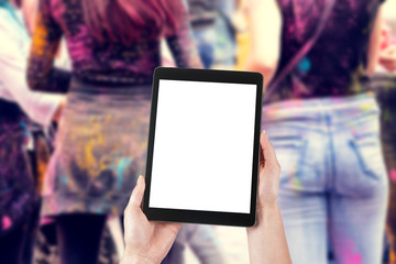 Woman's hands are holding a tablet with a blank screen and a copy space and in the background a party for young people.