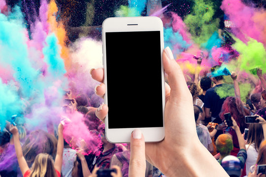 Woman's hands are holding a smartphone with a blank screen and a copy space and in the background a party for young people.