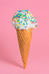 funny creative concept of close up wafer cup with ice cream and colorful sprinkles on pink background, copy space