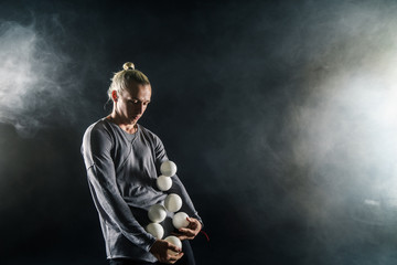 Fototapeta na wymiar Blond juggler with white balls on black background