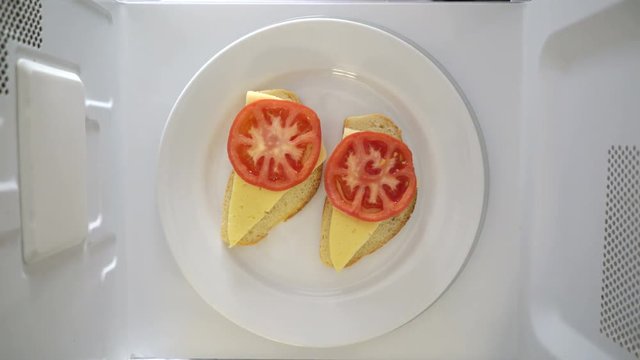 Making microwave breakfast meal. Sandwiches with melted cheese on white plate microwaving top view.