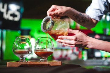 women's hands professionally barista pour the prepared drink into glass cups. championship among coffee houses, members of teams show barista's skill, prepare drinks, teamwork.