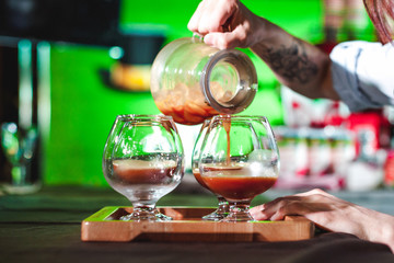 women's hands professionally barista pour the prepared drink into glass cups. championship among coffee houses, members of teams show barista's skill, prepare drinks, teamwork.