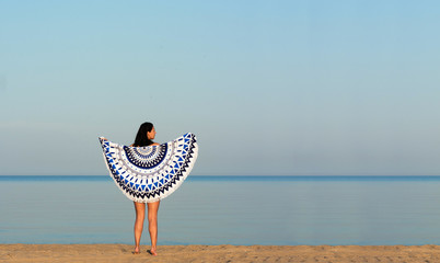 Pretty woman with a mandala round beach tapestry in the ocean coast.