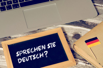Ein Computer, Flagge von Deutschland und eine Kreidetafel mit der Frage Sprechen Sie deutsch