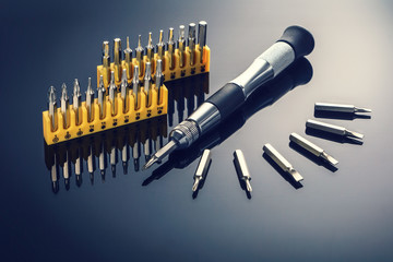 Tool set screwdriver with replaceable bits, on the gloss of black surface - obrazy, fototapety, plakaty