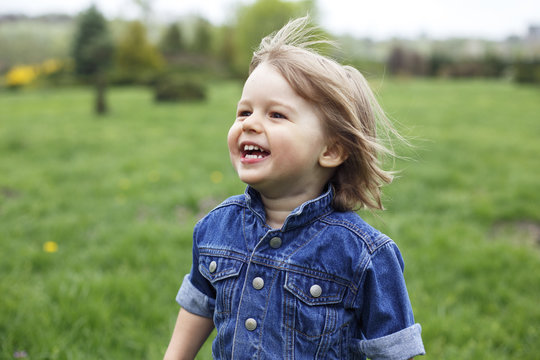 Outdoor portrait of a cute happy smiling young caucasian 1-2 years old toddler boy having fun running around in a park .