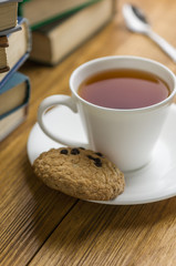 A cup of tea and some chocolate chip cookies over a books on a brown wooden table