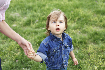 Family scene , closeup parent and baby holding hand together. Cute toddler boy with wondering face, looking up, holding mum's finger