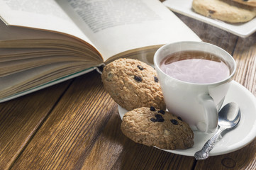 A cup of tea and some chocolate chip cookies over a books on a brown wooden table