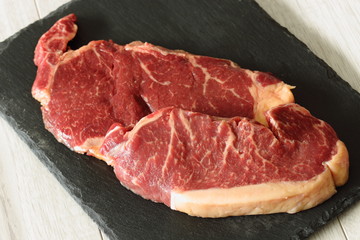 Sirloin steak beef joints on a slate cutting board on a grey wood background