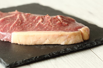 Sirloin steak beef joints on a slate cutting board on a grey wood background