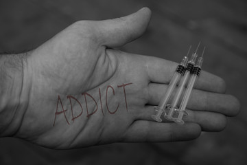 Man holding syringes needles with the word addict written on his hands with selective colour