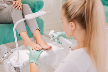 Some sanitizer. Blonde-haired chiropodist working hard while spraying some sanitizer on feet of client