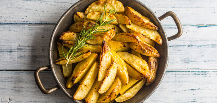 Roasted potatoes in a frying pan on wooden board