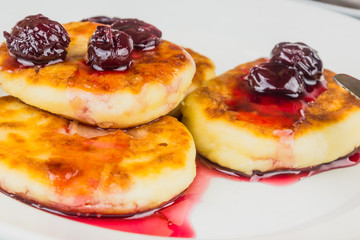 Russian cheesecakes with cherry jam on a white plate