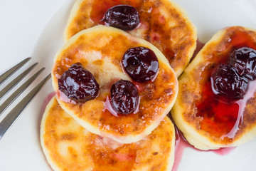 Russian cheesecakes with cherry jam on a white plate