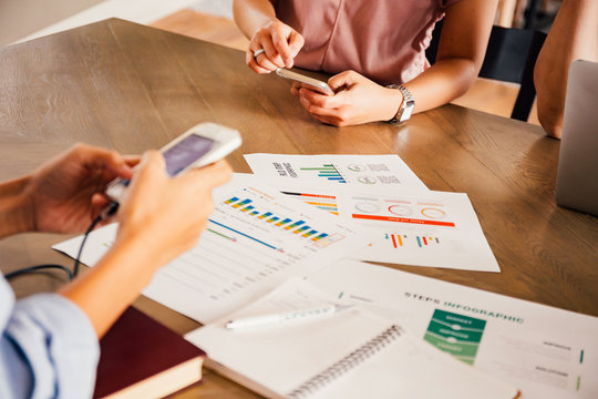 Group of people using a phone during meeting with notes and marketing data analysis papers