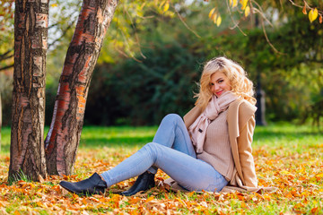 Young beautiful woman sitting on the ground coverd with fallen autumn leaves