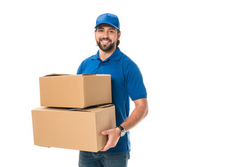 handsome happy young delivery man holding cardboard boxes and smiling at camera isolated on white