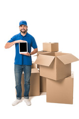 young delivery man holding digital tablet with blank screen and smiling at camera while standing near boxes isolated on white