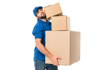 tired delivery man holding stacked cardboard boxes and looking at camera isolated on white