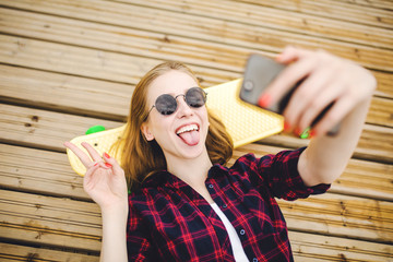Young stylish urban girl in hipster outfit making selfie while lying with on wooden pier