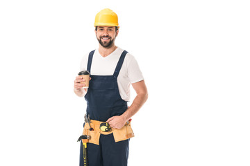 handsome happy workman in tool belt holding paper cup with coffee to go and smiling at camera isolated on white