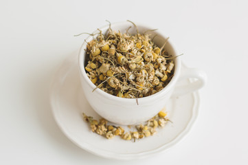 White tea cup with dried chamomile flowers on white background. Healthy herbal drink