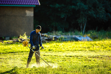 Young guy mows the grass trimmer