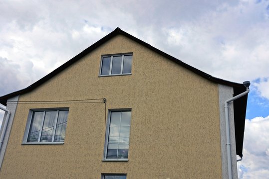 part of a gray brown house with windows against the sky and clouds