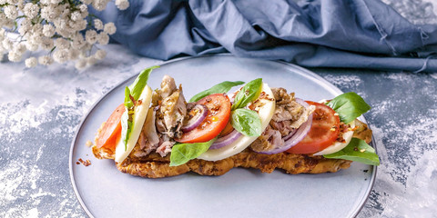 Mediterranean Kitchen. Sandwich with smoked chicken, mozzarella, tomatoes, sweet onions and basil leaves on a round plate on a concrete background. Close-Up