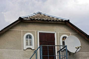 attic of a gray rural house with a door with windows and a satellite dish on the sky background