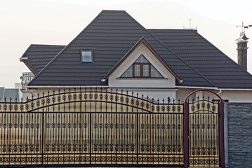 part of the fence with closed brown iron gates and a large private house