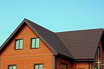 part of a large brick brown house with windows under a tiled roof on a sky background