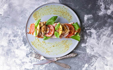 Italian sandwich with smoked chicken, mozzarella, tomatoes, sweet onions, basil leaves and pesto sauce on a round plate on a concrete background. Mediterranean Kitchen. Top view