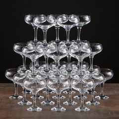 a lot of empty wine glasses on a brown table, built by a high pyramid, on a black background,...