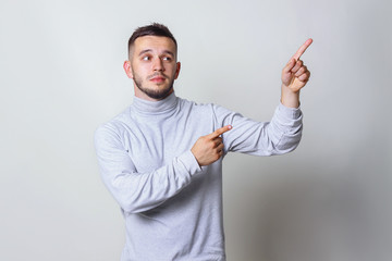 Young man pointing or show direction. The man points with both hands toward the left upper corner of the frame gray background copy space