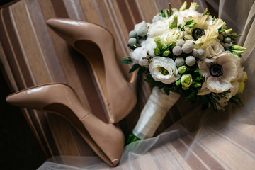 Pair of beautiful beige women's shoes. Nearby lies a bouquet of flowers. Probably the wedding day